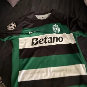 Sporting CP Gyökeres matchtröja Nike - Sporting CP fotbollströja med Gyökeres #9 på ryggen. Klassiska gröna och svarta breda ränder, vita detaljer och sponsortryck. Champions League-märke på ärmen. Tillverkad i lätt och ventilerande material, perfekt för match eller träning. Pris kan diskuteras:)