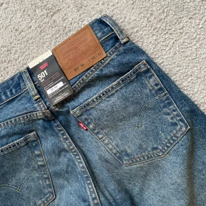 Levi's 501 blå jeans straight fit - Klassiska Levi's 501 jeans i blå tvätt med raka ben och låg midja. Jeansen har fem fickor, knappgylf och den ikoniska läderpatchen bak. Helt nya lappen kvar