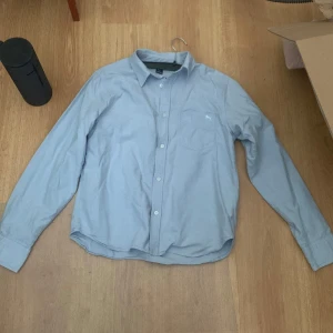 Ljusblå skjorta från H&M L.O.G.G. - Säljer en stilren ljusblå skjorta från H&M L.O.G.G. med klassisk krage och knäppning framtill. Skjortan har lång ärm, bröstficka med broderad häst och är gjord i mjuk bomull. Perfekt för dig som gillar enkel och clean stil.