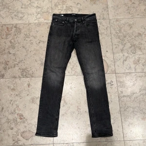 Jack & Jones Slim Glenn  - Svart-gråa slim fit jeans från Jack & jones i storlek 28/32 Slim Glenn. Jeansen har klassisk femficksdesign, svarta sömmar och en snygg tvättad finish. Perfekta för dig som gillar en smalare passform och stilren look.