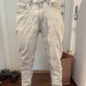 Ljusgrå jeans med tapered fit - Säljer ett par ljusgrå jeans med klassisk femficksdesign och avsmalnande ben. Jeansen har bälteshällor, knappgylf och är tillverkade i ett mjukt bomullstyg. Perfekta för dig som gillar en avslappnad men ändå stilren look.