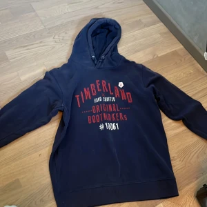 Marinblå hoodie från Timberland - Säljer en marinblå hoodie från Timberland med röd och vit text på bröstet. fin kvalité storlek M