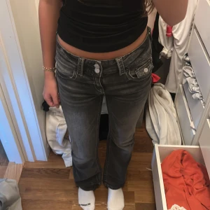 Grå bootcut jeans från Gina Tricot - Snygga grå jeans från Gina Tricot i bootcut-modell med markerade sömmar och dubbla knappar i midjan. Jeansen har klassiska fickor fram och bak samt cool tvättad look. Perfekta för dig som gillar en trendig och avslappnad stil.