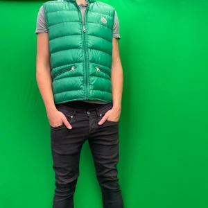 Moncler väst - Snygg grön dunväst från Moncler med quiltad design och dragkedja framtill. Västen har två fickor med dragkedja och klassisk Moncler-logga på bröstet. Perfekt att slänga över en hoodie eller t-shirt för en cool look. Använd 2-3 gånger köpte den för 3999kr