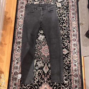 Mörkgrå skinny jeans från Lee - Snygga mörkgrå jeans från Lee med klassisk femficksdesign och skinny passform. Jeansen har bälteshällor, dragkedjegylf och Lee-logga på bakfickan. Perfekta för dig som gillar en smal siluett och stilren look.