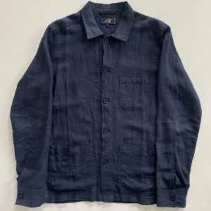 Mörkblå overshirt från SIR - Stilren mörkblå overshirt i linne med klassisk krage och tre fickor framtill. Skjortan har knäppning med matchande knappar och lång ärm. Perfekt för en avslappnad men snygg look. nypris 2000kr.