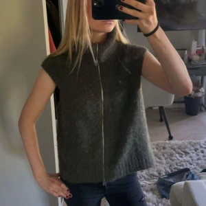 Mörkgrå stickad väst med dragkedja - Snygg mörkgrå stickad väst med hög krage och hel dragkedja framtill. Västen är ärmlös och har en lite loose passform.