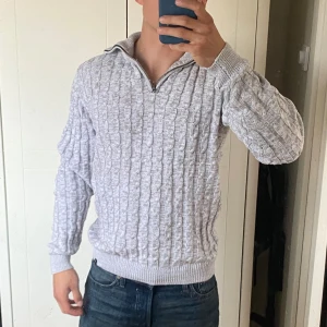 Grå ribbstickad halfzip med dragkedja - Säljer en mysig grå stickad tröja med dragkedja vid halsen. Perfekt för kyliga dagar med sitt ribbade mönster och långa ärmar. Passar både till vardags och lite finare tillfällen. Superbekväm och stilren!