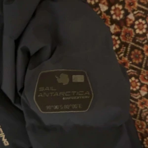 Mörkblå dunjacka Sail Racing 160 - Snygg mörkblå dunjacka från Sail Racing med huva och coola detaljer som Sail Antarctica Expedition-patch på ärmen. Jackan har flera praktiska fickor med dragkedja och en stilren design som passar dig som gillar äventyr och streetwear.nypris:2500 köpt på black friday 