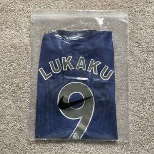 Manchester United Lukaku bortatröja Adidas - Snygg marinblå Manchester United bortatröja från Adidas med guldiga detaljer, Chevrolet-logga och klubbmärke på bröstet. Nummer 9 och LUKAKU på ryggen. Tillverkad i lätt och ventilerande Climalite-material, perfekt för fotboll eller att bära som supporter.