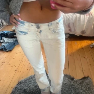 Vita jeansbyxor från Blue Jeans - Säljer ett par vita jeansbyxor från Blue Jeans med ljusblå slitningar vid fickorna. Byxorna har låg midja, raka ben och klassisk femficksdesign. Snygg metallogo bak på linningen och cool tvättad look. Perfekta för dig som gillar en fräsch och avslappnad stil.