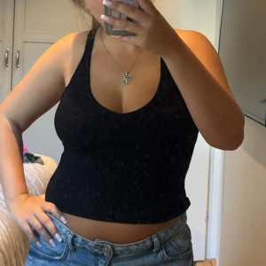 Svart ribbad linnetopp från BikBok - Svart ribbad skön linnetopp från BikBok med djup v-ringning och breda axelband. Toppen är croppad och har en tight passform som framhäver figuren. Perfekt att matcha med jeans eller kjol för en snygg och enkel look.