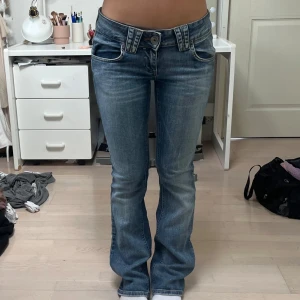 low waste bootcut jeans  - Säljer ett par blå lågmidjade jeans från Replay med bootcut-snitt. Jeansen har snygga detaljer vid fickorna, dubbla bälteshällor och klassisk knappstängning. Materialet är jeans i bomull med lätt slitning för en cool look.