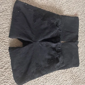 Svarta bootcut jeans från Lauren Jeans Co - Svarta jeans från Lauren Jeans Co Ralph Lauren i bootcut-modell med breda ben. Jeansen har snygga broderade blommor ton-i-ton på framsidan och är gjorda i bomull. Perfekt för dig som vill sticka ut med coola detaljer och bred siluett.