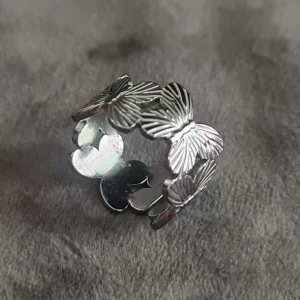 Silvrig ring med fjärilar - Unik silvrig ring med flera detaljerade fjärilar runt hela bandet. Ringen har en öppen baksida som gör den justerbar och fjärilarna har snygga linjer som ger extra cool effekt. Perfekt för dig som vill ha något annorlunda och trendigt.
