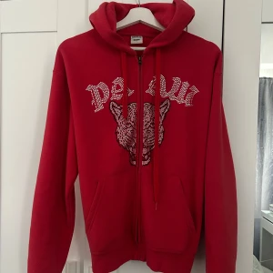 Röd hoodie med strasstenar och tryck - Säljer en röd hoodie från paaw med dragkedja och glittriga strasstenar. Tröjan har huva  och två fickor framtill. Pris kan diskuteras!!!