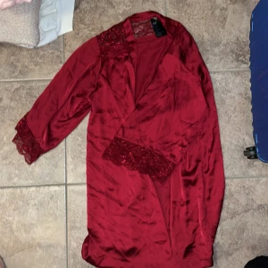 Röd spet morgonrock från H&M XS/S - Snygg röd morgonrock från H&M i glansig polyester med spetsdetaljer vid axlar och ärmslut. Omlottmodell med trekvartsärm, perfekt för dig som vill sticka ut. Klänningen har en elegant och feminin look.