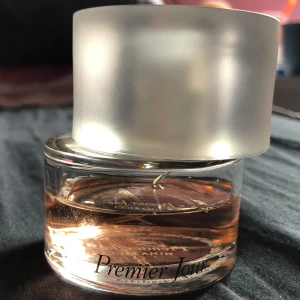 Nina Ricci Premier Jour parfym - Premier Jour från Nina Ricci är en elegant parfym i en rund glasflaska med frostad, silvrig kork. Doften har en ljusrosa vätska som syns genom det klara glaset. Flaskan har en modern och stilren design med svart text på framsidan. Doften av parfymen är sexig, fräsch och även lite söt. Det är mer än hälften kvar! Skulle säga ungefär 40 av 50 ml kvar ungefär.