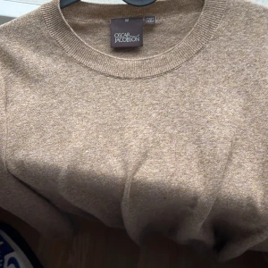 Beige stickad tröja Oscar Jacobson - Snygg beige stickad tröja från Oscar Jacobson i  modellen custer round neck. Perfekt för lager-på-lager och funkar lika bra till jeans som till chinos. Mjuk och skön känsla tack vare det stickade materialet. Nypris 1200kr, säljer pga för liten. Skriv vid frågor/intresse!