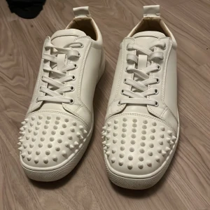 Vita loubs med spikar - Säljer ett par vita sneakers från Christian Louboutin med ikonisk röd sula och coola nitar över tån. Skorna har snörning och är tillverkade i skinn, perfekt för dig som vill sticka ut med din stil. Jag säljer för att de inte passar mig längre.