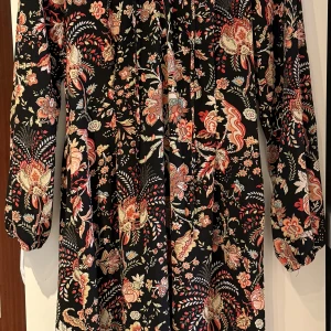 Svart blommig långklänning från H&M - 🌸Klänning med färgglatt blommönster och knyt i halsen. Klänningen har långa ärmar och ett vackert fall. Storleken är 36 men passar även 38 enligt mig 🌸