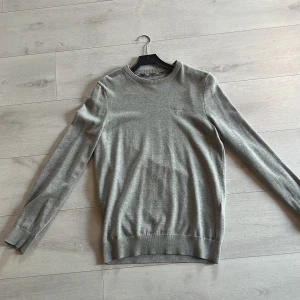 Grå stickad tröja från Barbour - Säljer en klassisk grå stickad tröja från Barbour med rund halsringning och diskret broderad logga på bröstet. Använd 5-10 gånger men är som ny! 