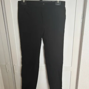 Svarta kostymbyxor från Mango - Säljer ett par klassiska svarta kostymbyxor från Mango Basics. Byxorna har en rak passform och är perfekta för en stilren look. De är tillverkade i ett mjukt material och har en enkel design utan synliga detaljer.