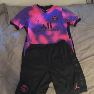 PSG x Jordan Neymar Jr fotbollströja XL - Säljer en PSG x Jordan Neymar Jr matchtröja i XL. Tröjan har korta ärmar och är i ett unikt rosa och lila mönster med svarta detaljer. PSG-logga, Jordan-logga och sponsortryck på bröstet, samt Neymar Jr och nummer 10 på ryggen. Materialet är lätt och andas.