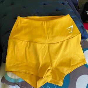 Gula träningstights shorts från Gymshark - Korta gula shorts från Gymshark. Perfekta för träning eller löpning nu i sommar. Mjukt och stretchigt material samt logga framtill. Knappt använda.