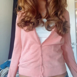 Ljusrosa kofta med knappar - Supersöt ljusrosa kofta med knappar framtill och lång ärm. Perfekt att slänga över ett linne eller t-shirt. Koftan har en enkel och clean look som passar till jeans eller kjol. Mjuk och tunn i materialet, vilket gör den skön att bära under vår och sommar.