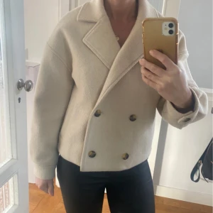 Beige kappa från Soaked in Luxury - Säljer en stilren beige kappa från Soaked in Luxury i storlek XS. Jackan har dubbelknäppning med stora knappar, bred krage och raka fickor. Perfekt för dig som gillar en klassisk och tidlös look.
