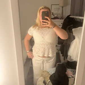 Vit spetsblus från Lindex - Säljer en söt vit spetsblus från Lindex med korta ärmar och rund halsringning. Blusen har ett fint blommigt spetsmönster och en lätt utsvängd volang nertill. Perfekt att styla med jeans eller kjol!