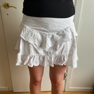Vit volangkjol med spets - Superfin vit kortkjol med volanger och broderad spetsdetalj. Kjolen är i bomull och har dragkedja i sidan. Perfekt fin kjol nu till sommarn! Skriv för frågor eller funderingar😊   Midjemått rakt över: 36cm                                     Längd: 37cm