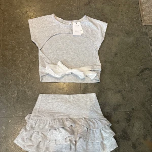 Ljusgrå volangkjol med matchande topp - Supersöt ljusgrå kjol med dubbla volanger och resår i midjan. Kjolen är i mjukt bomullsmaterial och har en kort längd. Perfekt att matcha med den tillhörande toppen med knytband framtill. Settet är från subdued, har aldrig använt det! Har kvar prislappen på tröjan som kostar 264kr tror att kjolen kostar ca 300 egentligen🫶🏼 hör av er för fler bilder!