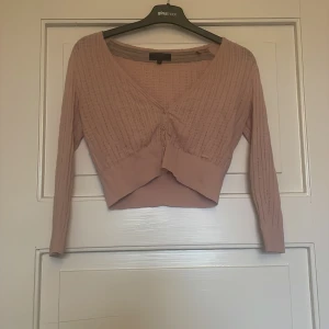 Ljusrosa croppad kofta från Guess - Supersöt ljusrosa croppad kofta från Guess med v-ringning och knappar framtill. Stickad i ett tunt, mönstrat material som känns både mjukt och luftigt. Perfekt att slänga över en topp för en trendy look!❤️❤️