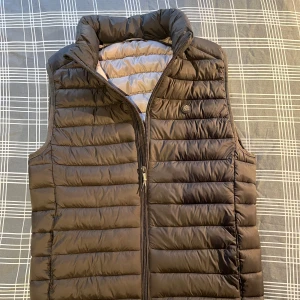 Grå dunväst från Springfield - Säljer en dunväst från Springfield i storlek XS. Västen har quiltad design, hög krage och dragkedja framtill. Perfekt för lager-på-lager och passar till många olika stilar.