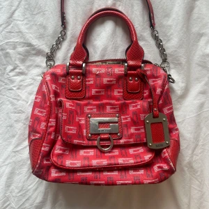 Vintage Guess röd axelväska  - Säljer min älskade röda guess väska! Säljer för den kommer inte till användning längre❤️den har några defekter som man kan se på de två sista bilderna! Eftersom väskan är mönstrad är det svårt att lägga märke till defekterna💋 Använd köp nu funktionen ❤️