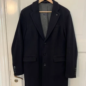 Svart rock med knappar - Stilren svart rock med klassisk krage och tre knappar framtill. Jackan har två fickor med lock och en bröstficka. Perfekt för kyligare dagar och ger en tidlös look.