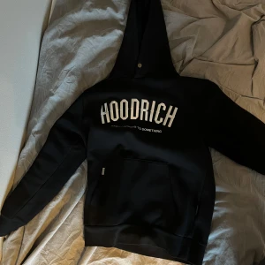 Knappt använd hoodie i mycket bra skick - Säljer en svart hoodie från Hoodrich med vit logga och texten 'FROM NOTHING TO SOMETHING' på bröstet. Tröjan har huva med snörning och en stor magficka framtill. Perfekt för en avslappnad stil.