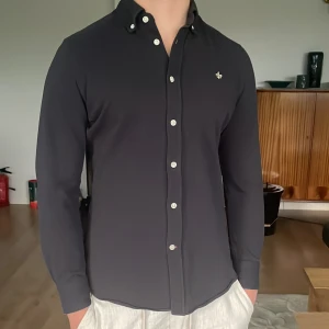 Blå Morris skjorta - Säljer en stilren blå skjorta från Morris med vita knappar och diskret logga på bröstet. Skjortan har lång ärm och klassisk krage, perfekt för en dressad look. Tillverkad i bomull för en skön känsla.