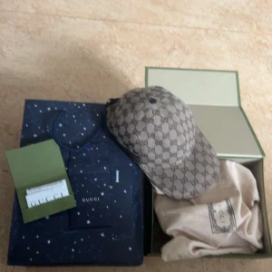 Gucci keps med monogrammönster - Snygg keps från Gucci med klassiskt GG-monogram i beige och brunt. Kepsen har böjd skärm och justerbar baksida. Ikoniska gröna och röda detaljer på sidan. Perfekt accessoar för att lyfta din outfit. **ALLA ORIGINELLA TILLBEHÖR MEDFÖLJER** Priset är inte hugget i sten!
