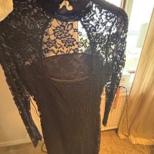 Svart spetsklänning från H&M - Supersnygg svart klänning från H&M med långärmade spetsdetaljer och blommigt mönster. Klänningen har hög hals, figurnära passform och transparenta partier upptill. Perfekt för dig som vill sticka ut med en elegant look. Skriv om ni vill ha bild på hur den sitter på💗