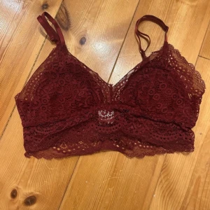 Vinröd spets bralette från Åhléns - Säljer en vinröd bralette i spets från Åhléns. Toppen har tunna axelband, vacker spetsdetalj och är fodrad framtill. Perfekt för att ge en romantisk touch till din outfit. Bh/topp