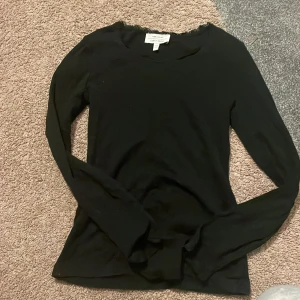 Svart spetsdetaljerad topp & Other Stories - Svart långärmad topp från & Other Stories Paris Atelier, med fina spetsdetaljer vid halsringningen. Tunn, ribbad och stretchig i materialet, perfekt för lager-på-lager eller som den är. Snygg och enkel att styla till olika looks. Lappen är lite sönder men går att laga snabbt 