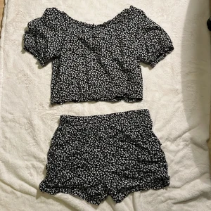 Blommig croppad topp från XOXO Friends - Supersöt croppad topp från XOXO Friends med svart botten och små vita blommor. Toppen har offshoulder-modell, korta puffärmar och vågig kant nertill. Perfekt för dig som gillar en lekfull och trendig stil.