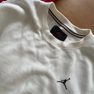 Jordan hoodie I rött och svart och vit Jordan sweatshirt. - Två snygga tröjor från Jordan: en vit sweatshirt med svart logga och tryck på ryggen, samt en röd och svart hoodie med broderad logga, huva och half zip. Båda har sportig vibe och är perfekta för streetwear. Storlek 13-15 år 163-175 cm