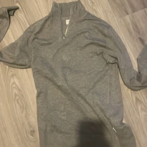 Grå tröja halfzip från Lindbergh - Säljer en stilren grå tröja från Lindbergh med dragkedja vid halsen. Perfekt för kyligare dagar med sin mjuka och bekväma passform. Tröjan har långa ärmar och ribbade detaljer vid krage och ärmslut. Kan tänkas gå ner i pris 