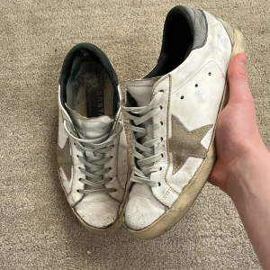 Golden Goose skor - Tja! Säljer nu dessa feta golden goose skor! De är i bra skick, men saknar box osv. Därför det låga priset! Storleken är 40, men kan passa upp till 41. Vid hälen har det gått bort lite tyg, men känns inte alls. Sulan är lite trasiga där bak, men går enkelt att fixa och märks inte. Utöver det så är skicket 7/10 skulle jag säga. Nypris: 5999kr❌‼️ Mitt pris: 1699kr✅ Skriv ifall du har frågor och pris kan diskuteras!🙌🤝