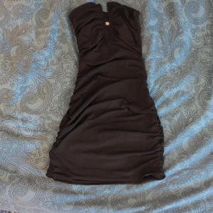 Svart kortklänning från Bershka - Säljer en svart tight kortklänning från Bershka med snygg v-ringning, strapless och med rynkade sidor som ger dig en fin figur. Klänningen har en tight passform men är tillverkad i ett mjukt material. 