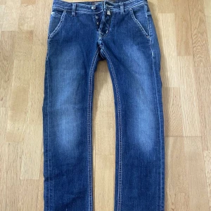 Blå jeans från Jacob Cohen - Säljer ett par klassiska blå jeans från Jacob Cohen i riktigt bra skick med raka ben och snygga slitningar. Jeansen har fem fickor, dragkedja och knapp i midjan samt läderpatch med logga bak. Perfekta för dig som gillar stilrena och tidlösa jeans. W30 men passar lite kortare eller längre. Pris kan diskuteras✅